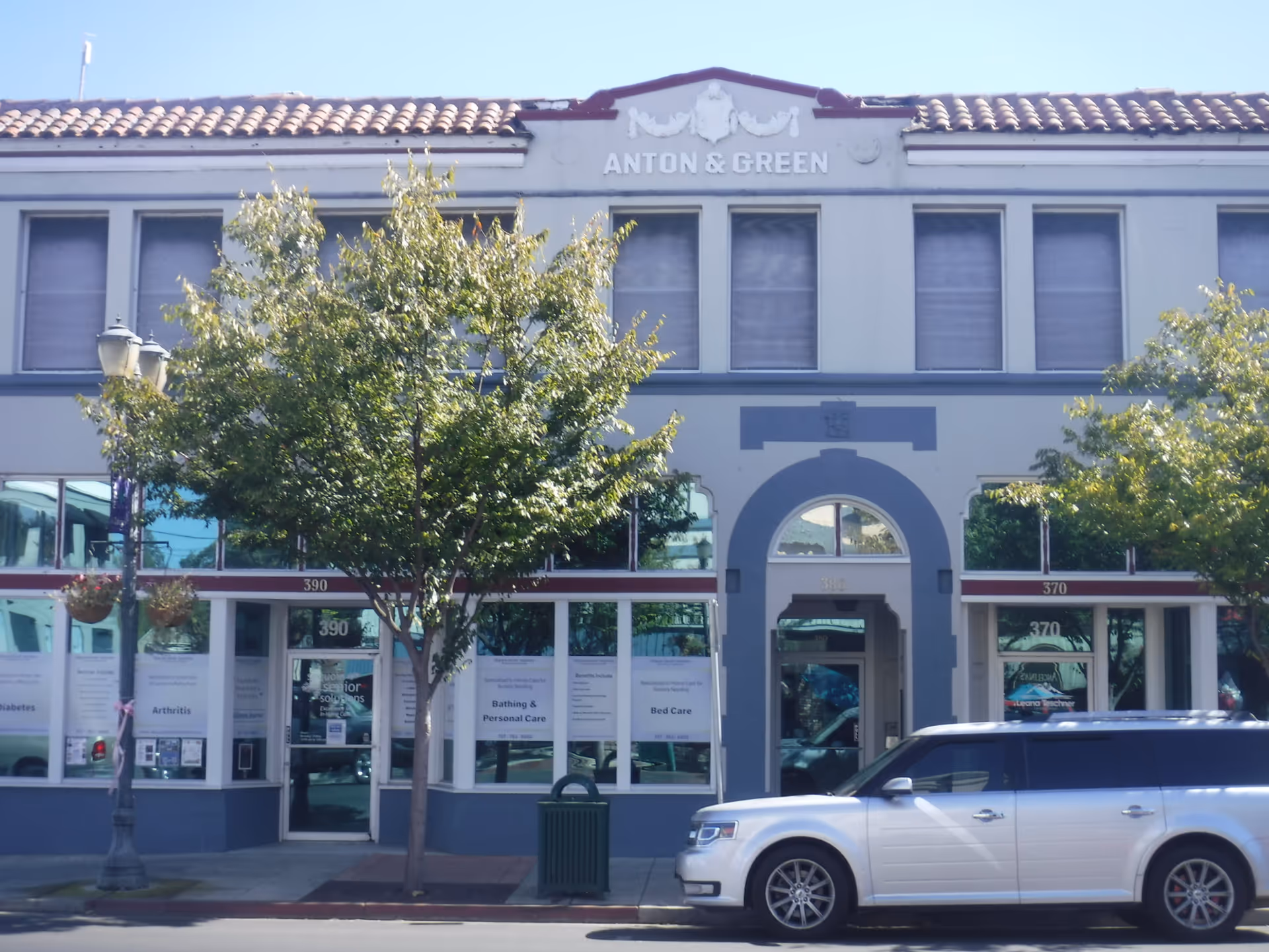 Exterior view of a senior facility storefront with trees and a parked SUV.