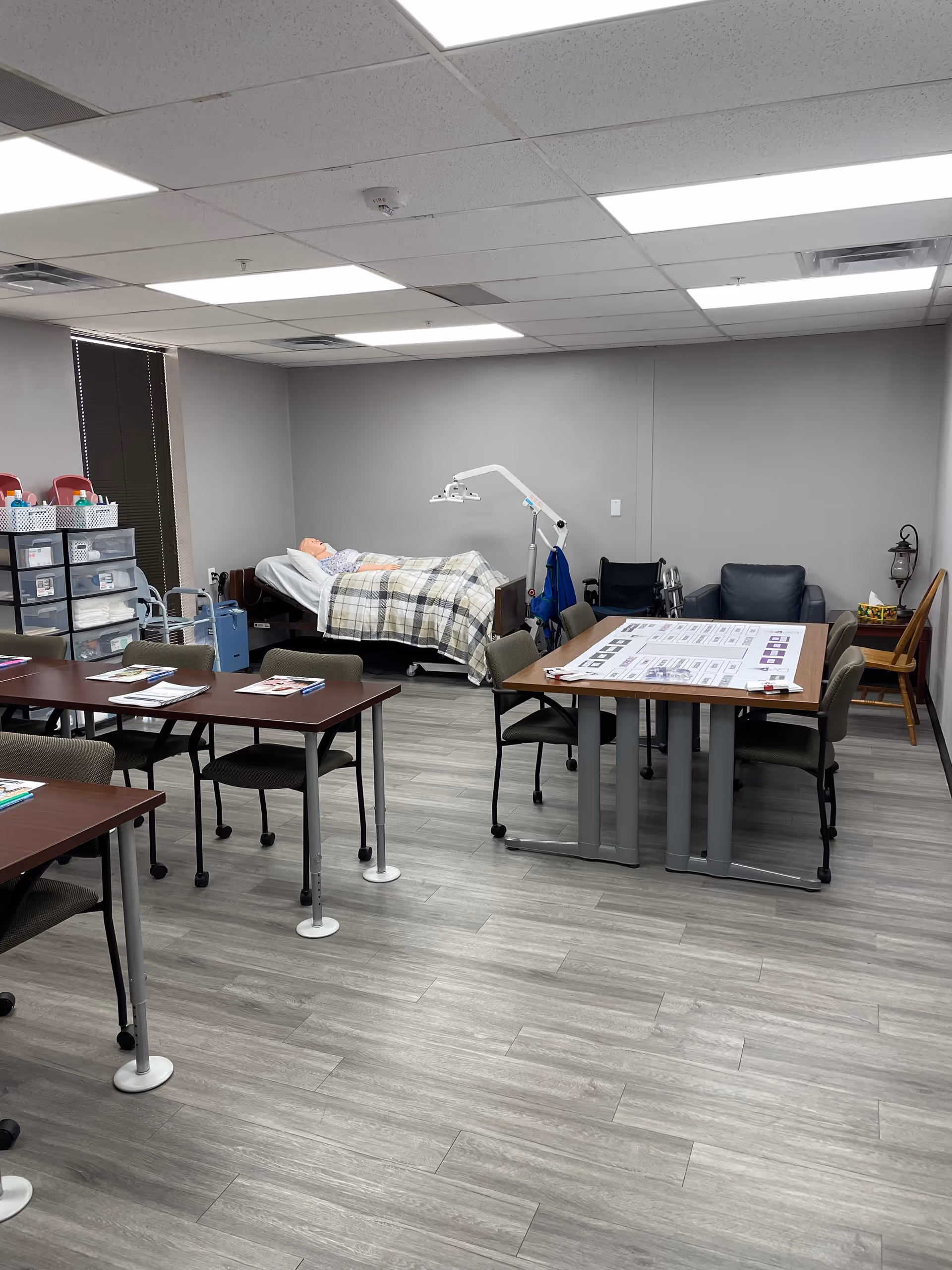 Interior training room in a senior facility with a bed, tables, and medical equipment.