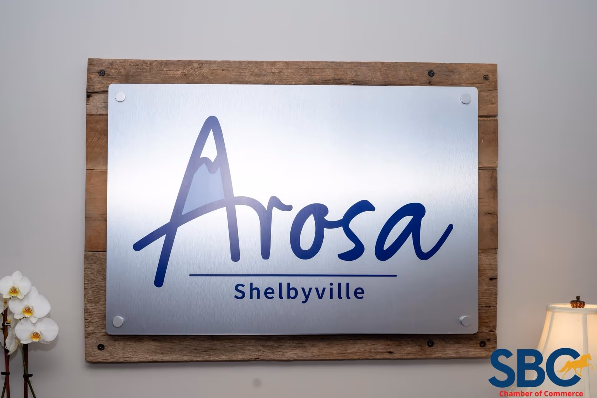 Metal sign reading Arosa Shelbyville mounted on a wooden panel in a lobby