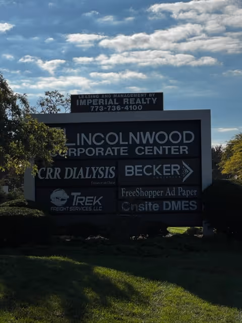 Outdoor signboard with multiple company names at Lincolnwood Corporate Center against a blue sky.