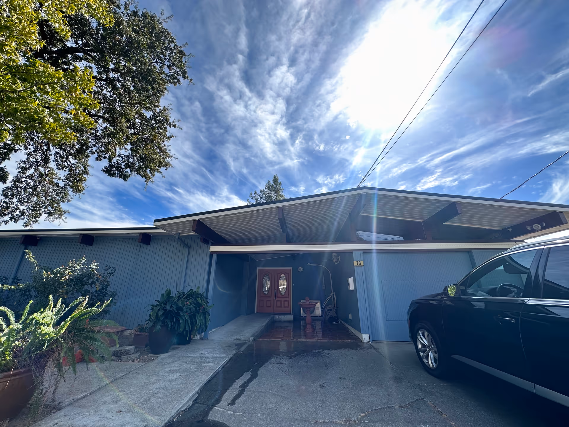 Blue building exterior with red double doors, driveway, and potted plants at entrance