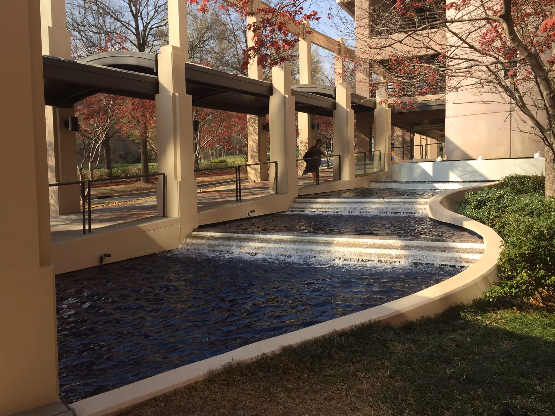 Outdoor walkway along a beige building with a curved water channel and trees