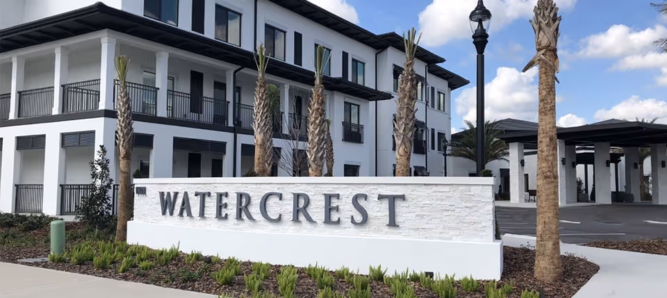Stone sign reading "WATERCREST" in front of a white multi-story building with palm trees and a covered entrance.