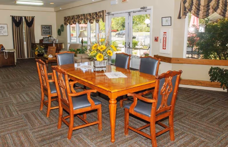 Wooden dining table with six chairs and sunflowers in a bright communal room