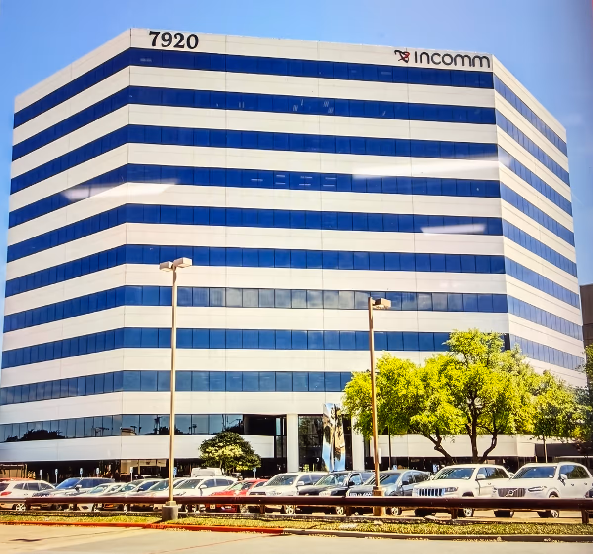 Tall modern office building with blue-tinted glass and a row of parked cars.