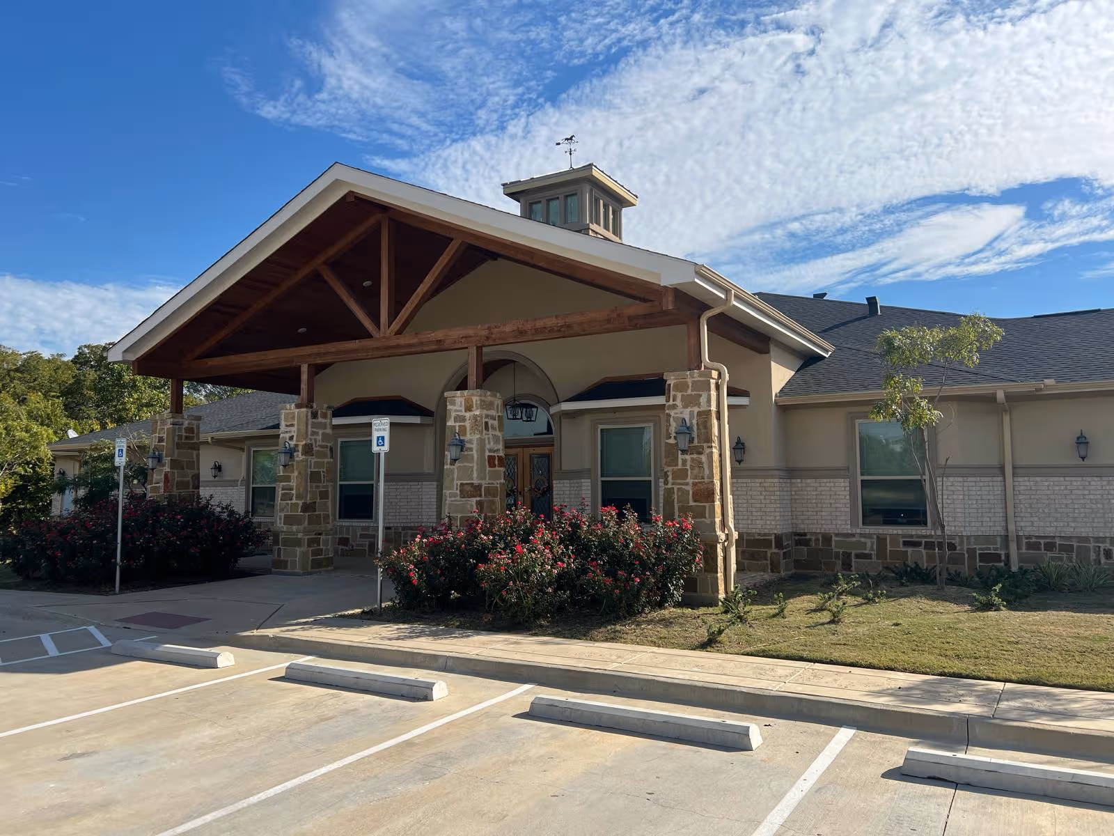 Village Green - Highland Village facility front with stone pillars, wooden portico, and landscaped entrance.