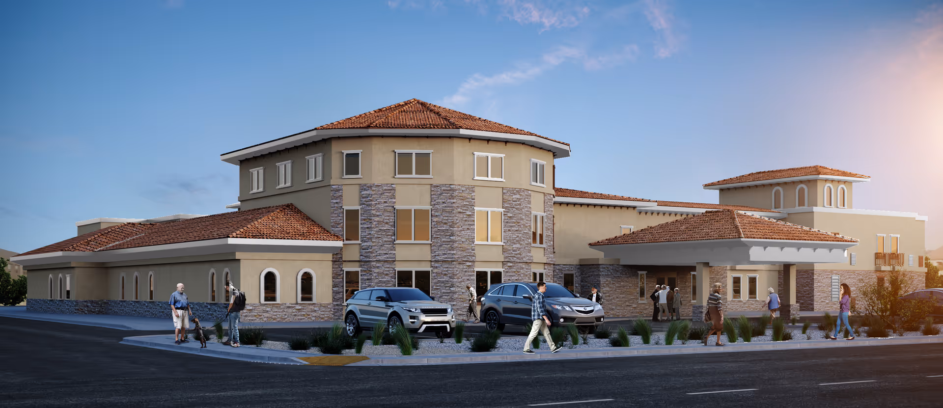 Exterior view of a large, modern senior living facility with beige walls, stone accents, and red-tiled roofs under a clear blue sky. Several people are walking on the sidewalk in front of the building, and cars are parked near the entrance.