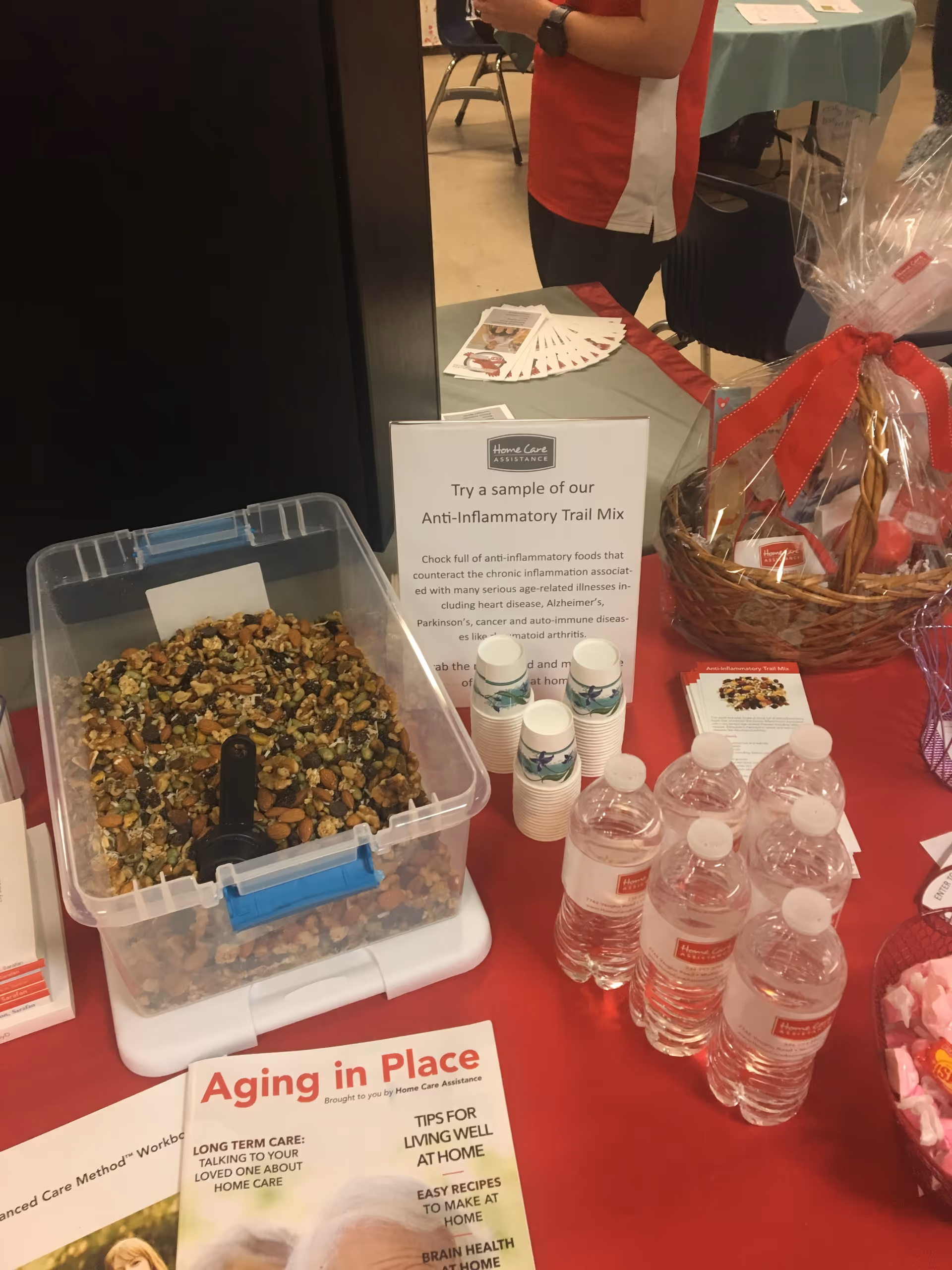 Table with trail mix, water bottles, and information at an indoor senior care event.