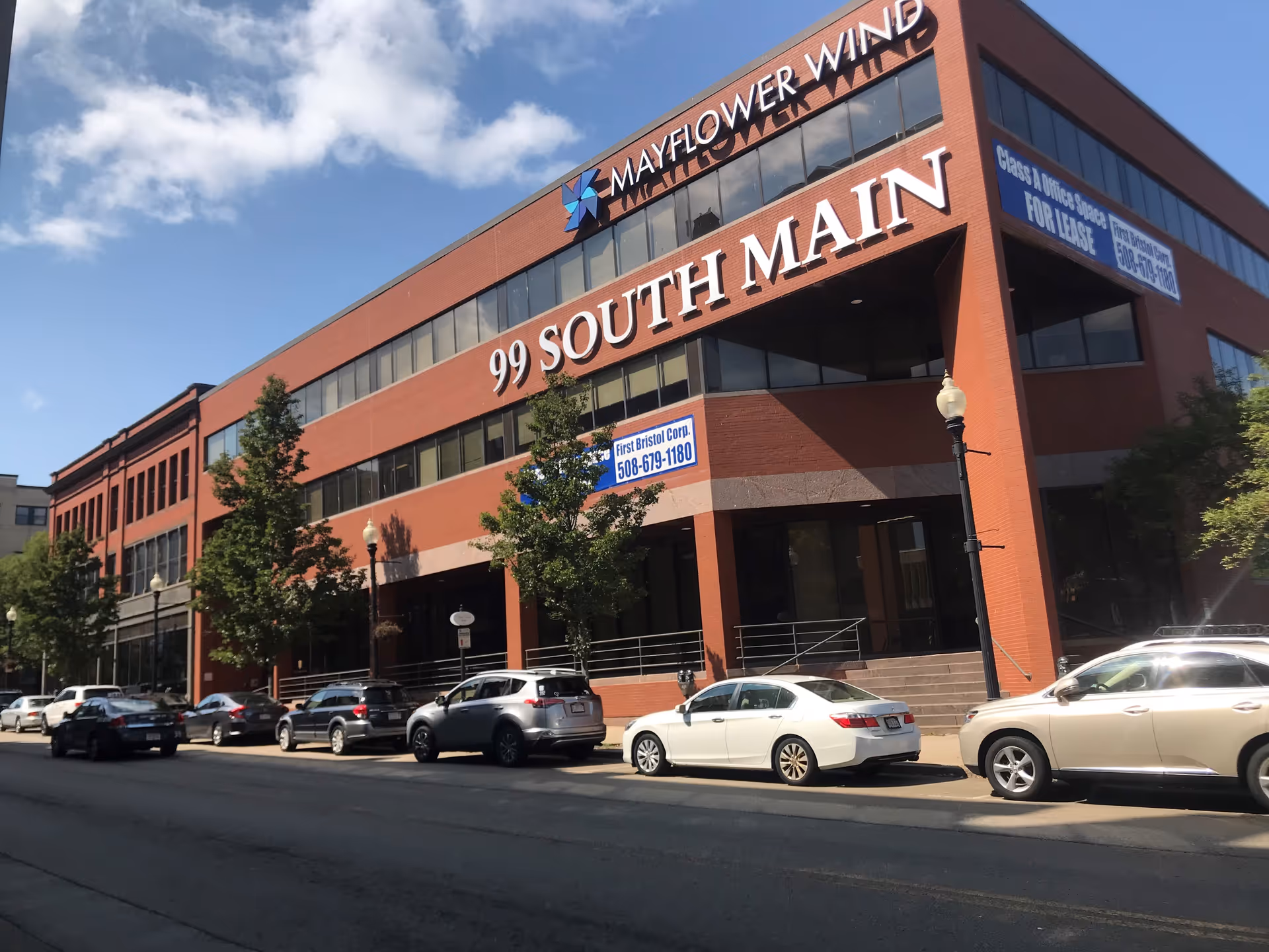 Exterior brick building with 99 South Main sign and cars parked along street.
