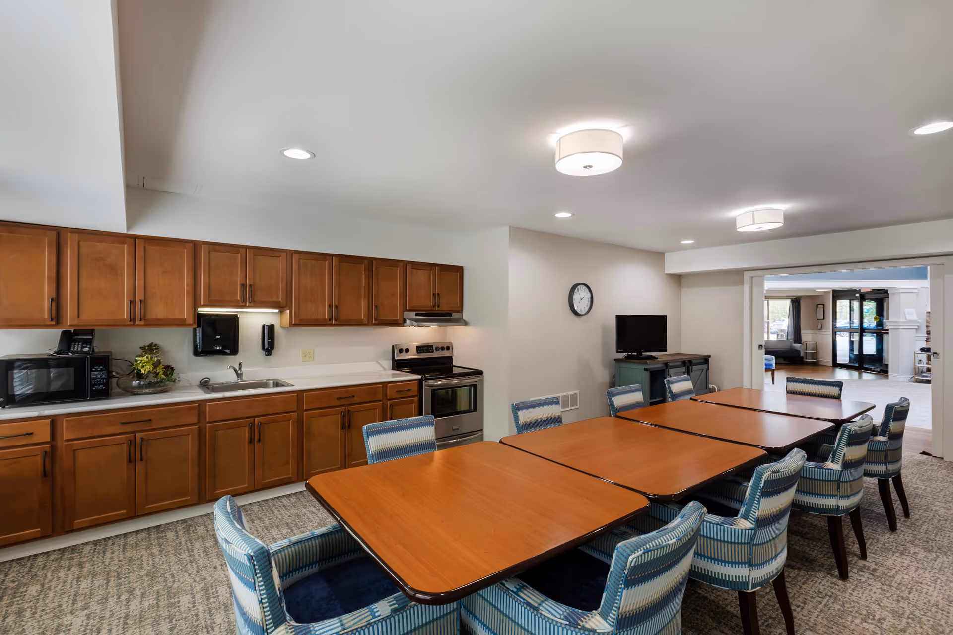 Communal kitchen and dining area with wooden cabinets, sink, and long table with blue chairs.
