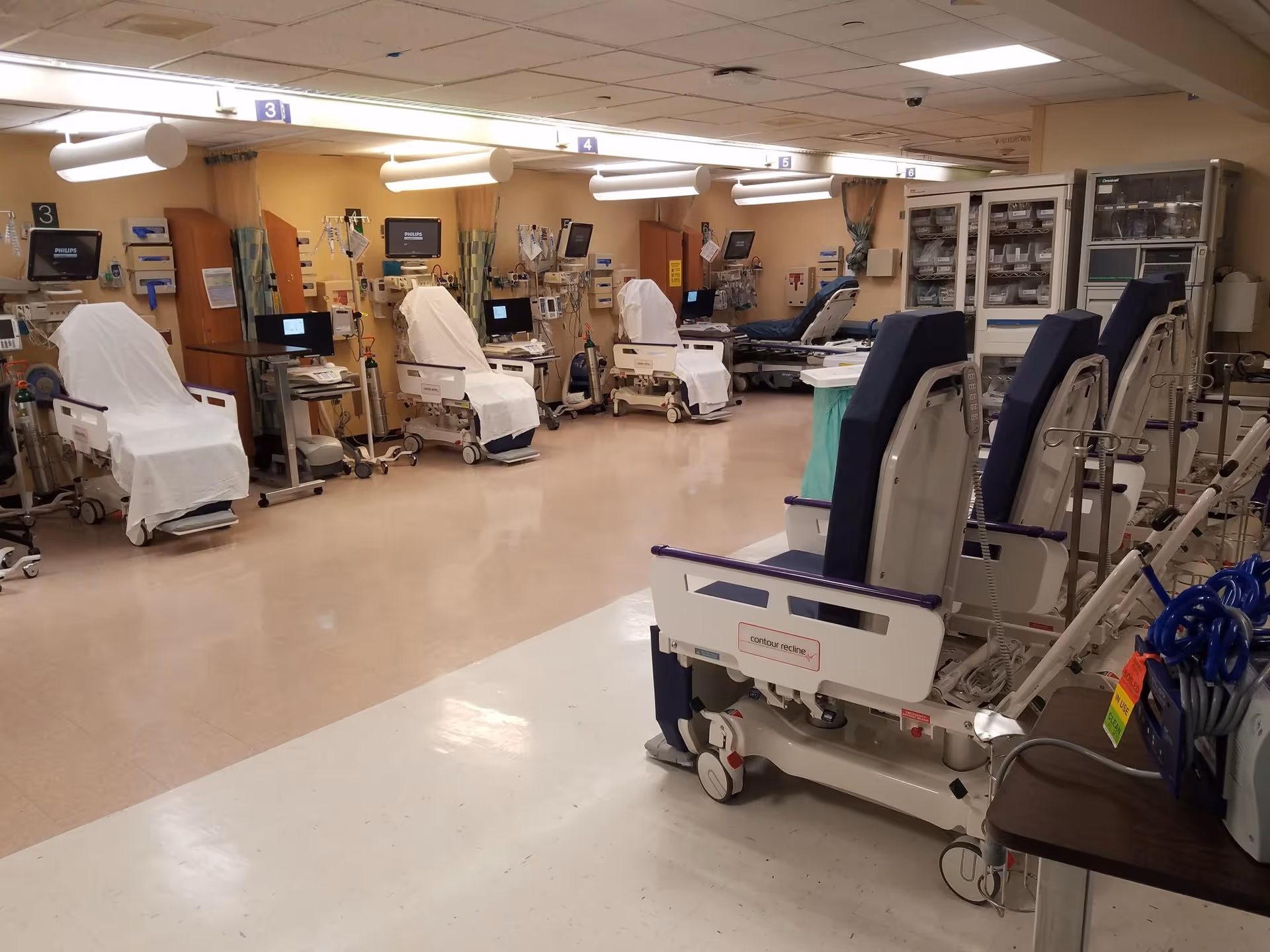 Hospital ward interior with multiple beds, monitors, and medical equipment.