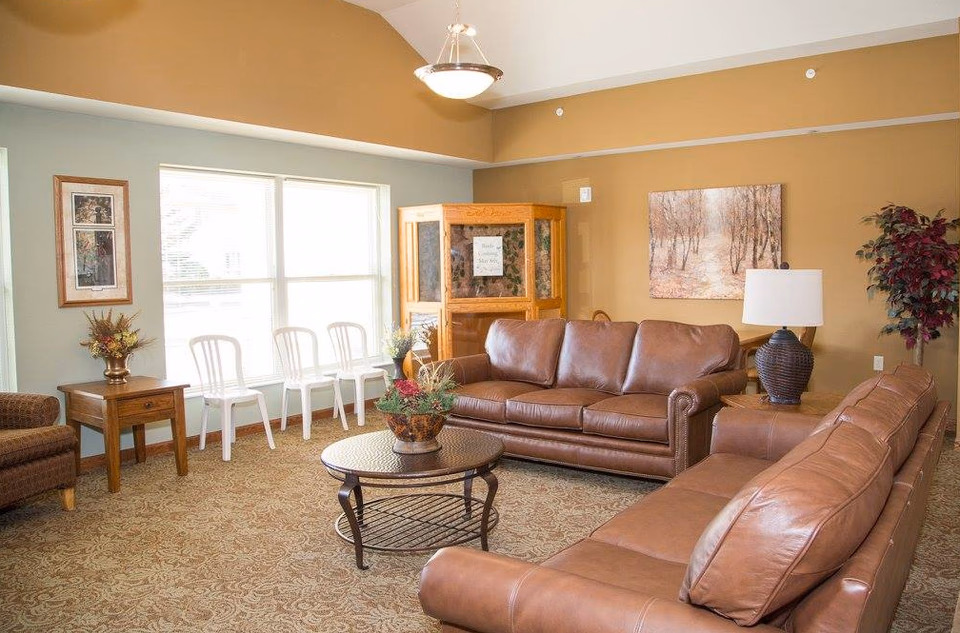 Senior living facility lounge with brown leather sofas and window seating.