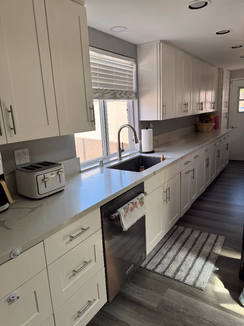 Modern kitchen in Fairweather Senior Facility with white cabinets, sink, window, and appliances.