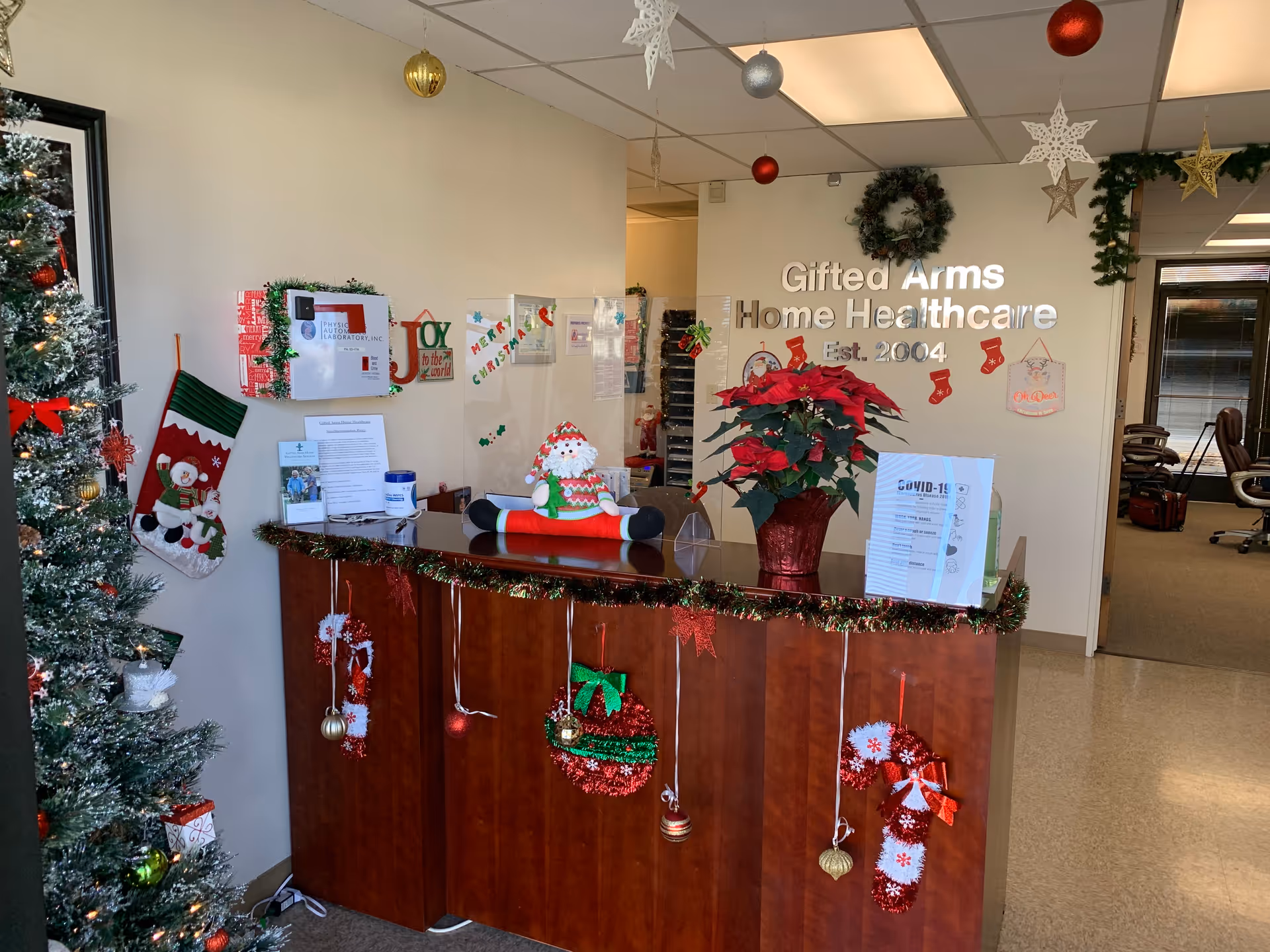 Lobby reception desk decorated for Christmas with a tree, garlands, stockings, and a Gifted Arms sign