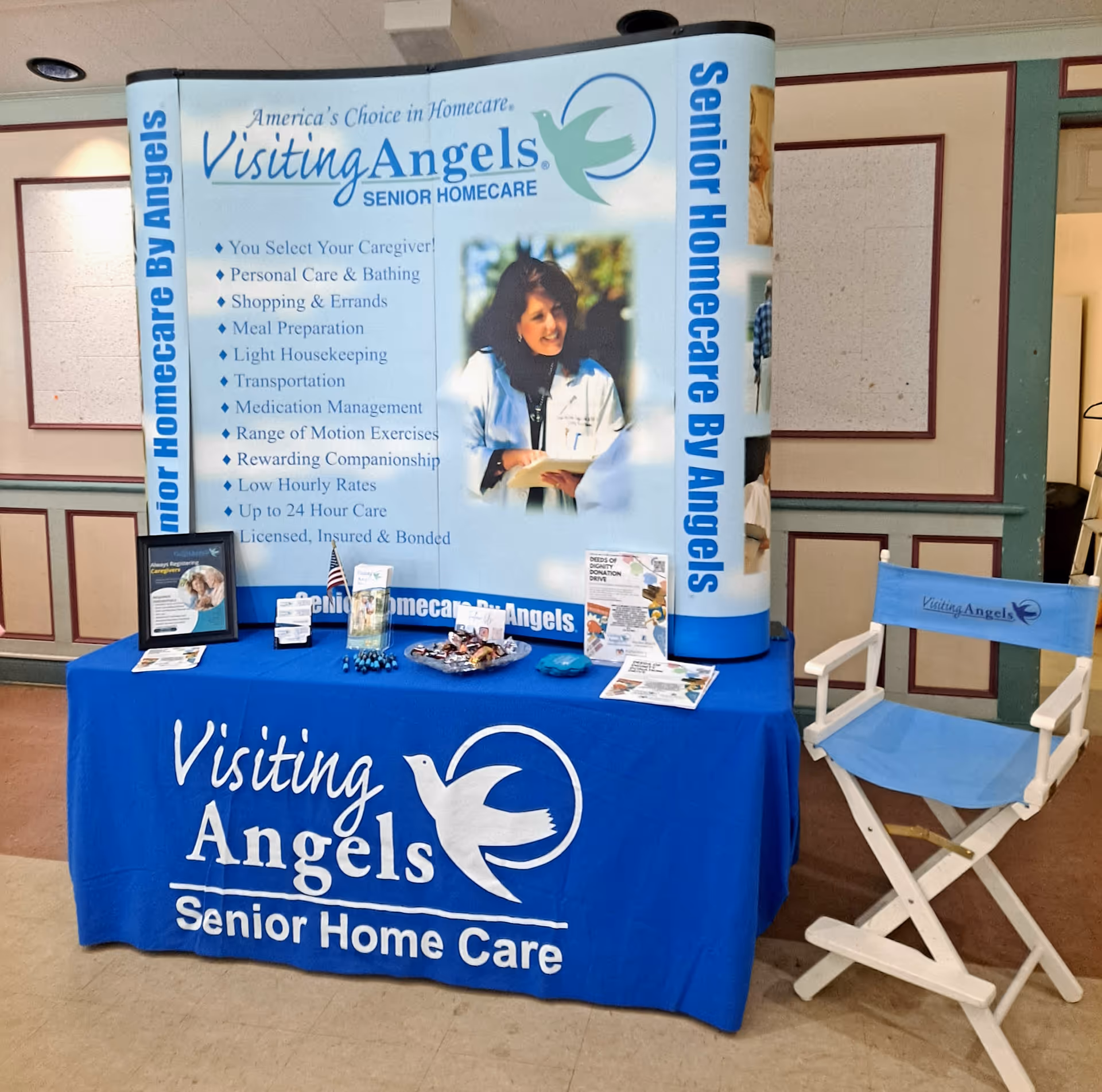 Indoor promotional booth for Visiting Angels Senior Home Care with blue banner and table.