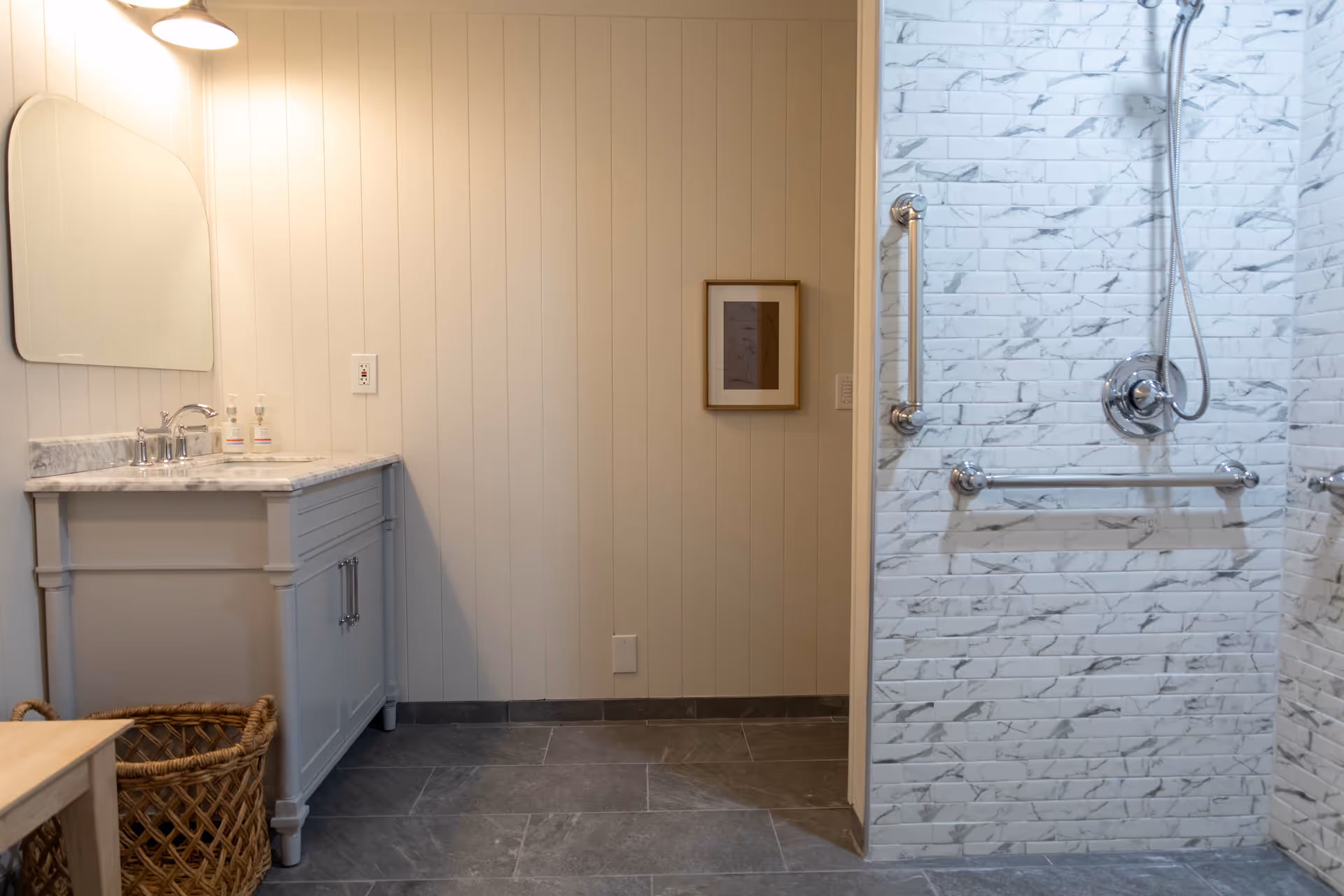 Bright bathroom with marble vanity, mirror, and accessible tiled shower with grab bars.