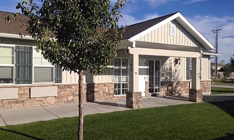 Exterior view of a single-story assisted living facility with a green lawn and tree.