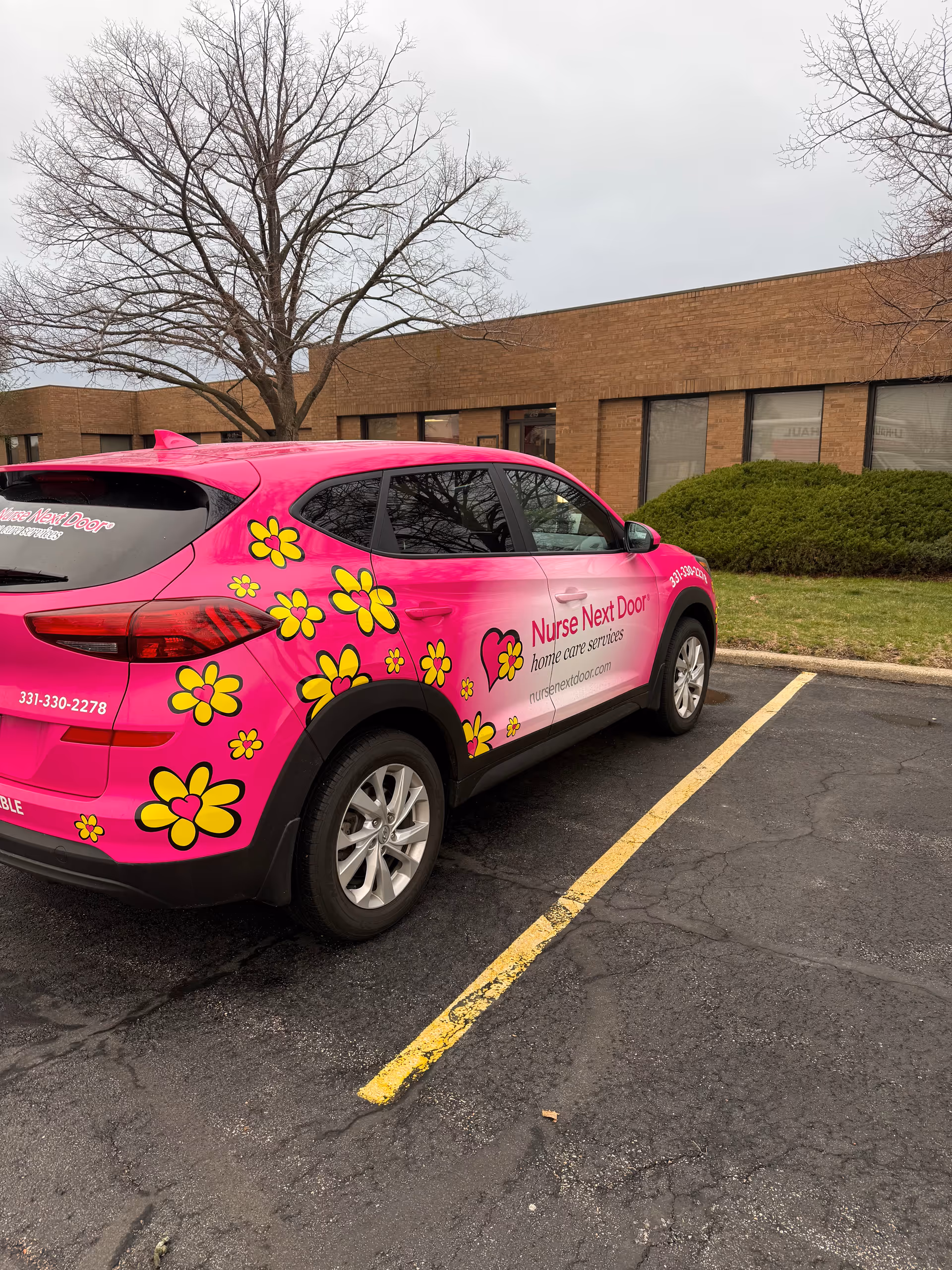 Pink Nurse Next Door van with flower decals parked outside a brick building.