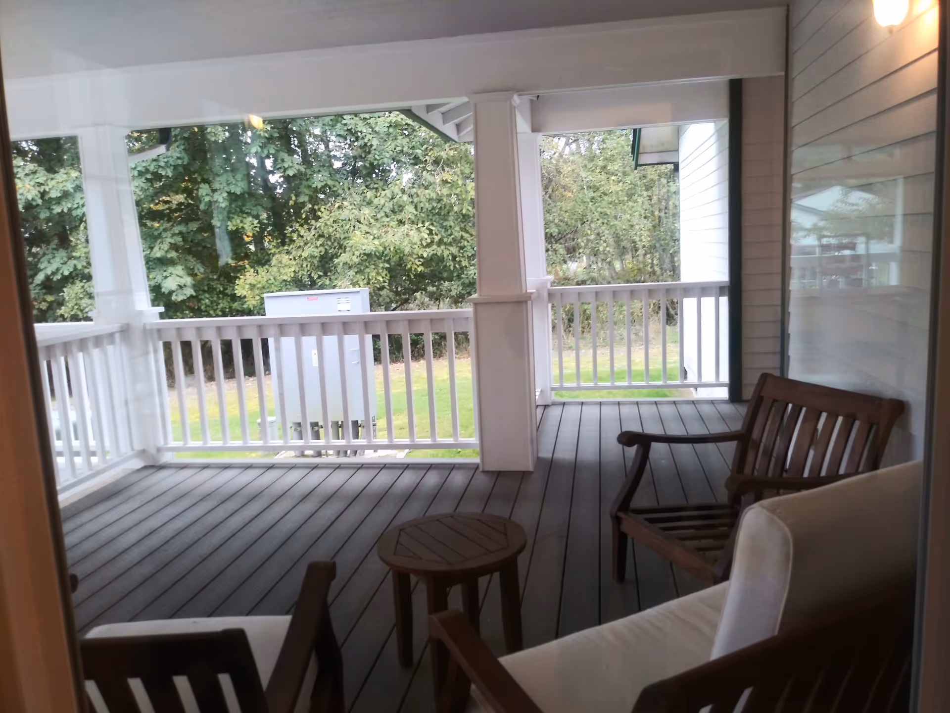 Covered porch with wooden chairs and a small table overlooking a green lawn.