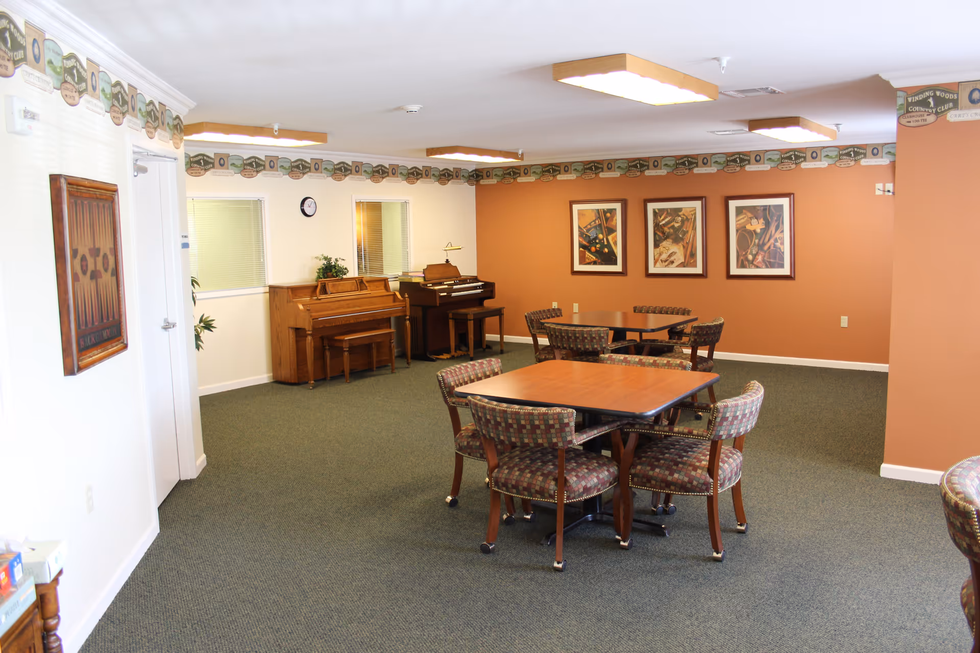 Common lounge area with round tables, upholstered chairs, and pianos against orange walls.