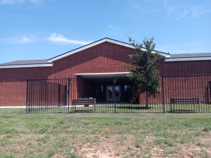 Brick senior living facility front entrance with black metal fence and gated entry