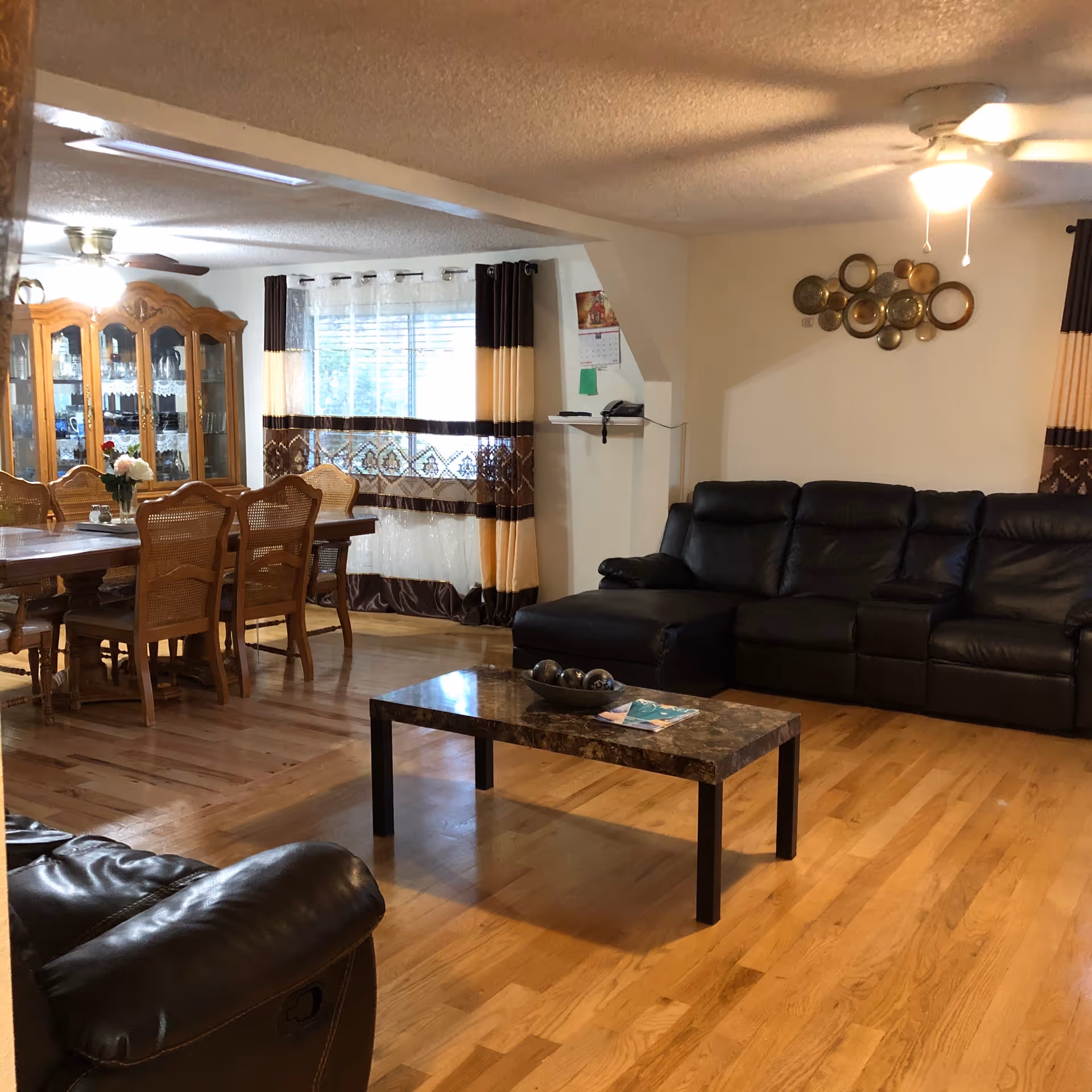 Spacious living area with black leather sofa, wooden dining table, and glass cabinet.
