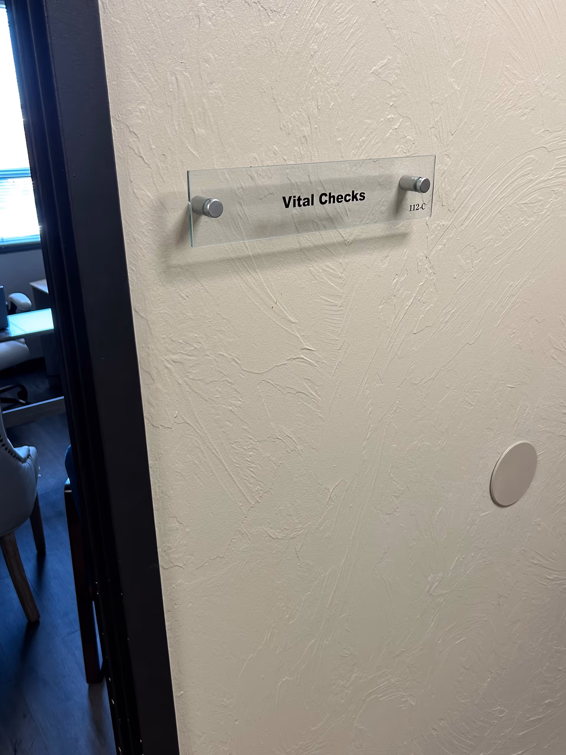 Glass nameplate on textured wall reading Vital Checks beside an open doorway.