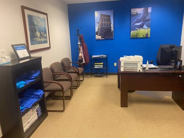 Office reception area with blue accent wall, row of chairs, and a desk with printer.