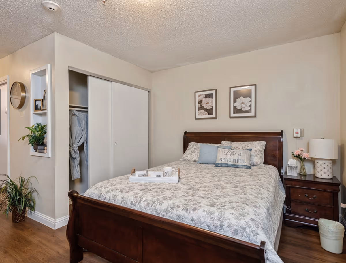 Neat bedroom with a wooden bed dressed in floral bedding, a nightstand with lamp and flowers, and a sliding-door closet.