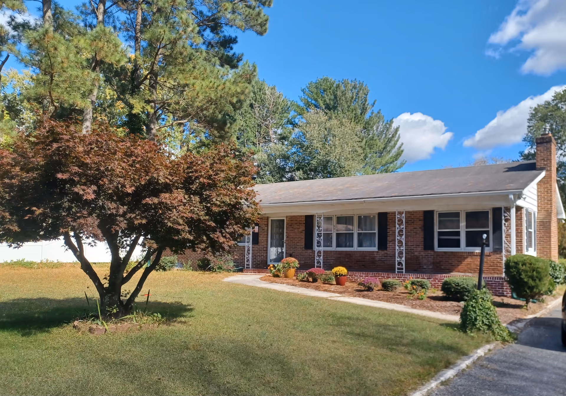 Single-story brick senior living facility with front entrance, well-kept lawn, tree, and potted flowers.