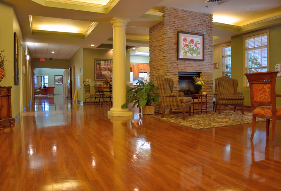 Spacious lobby lounge with a stone fireplace, wooden floors, and seating in a senior living facility.