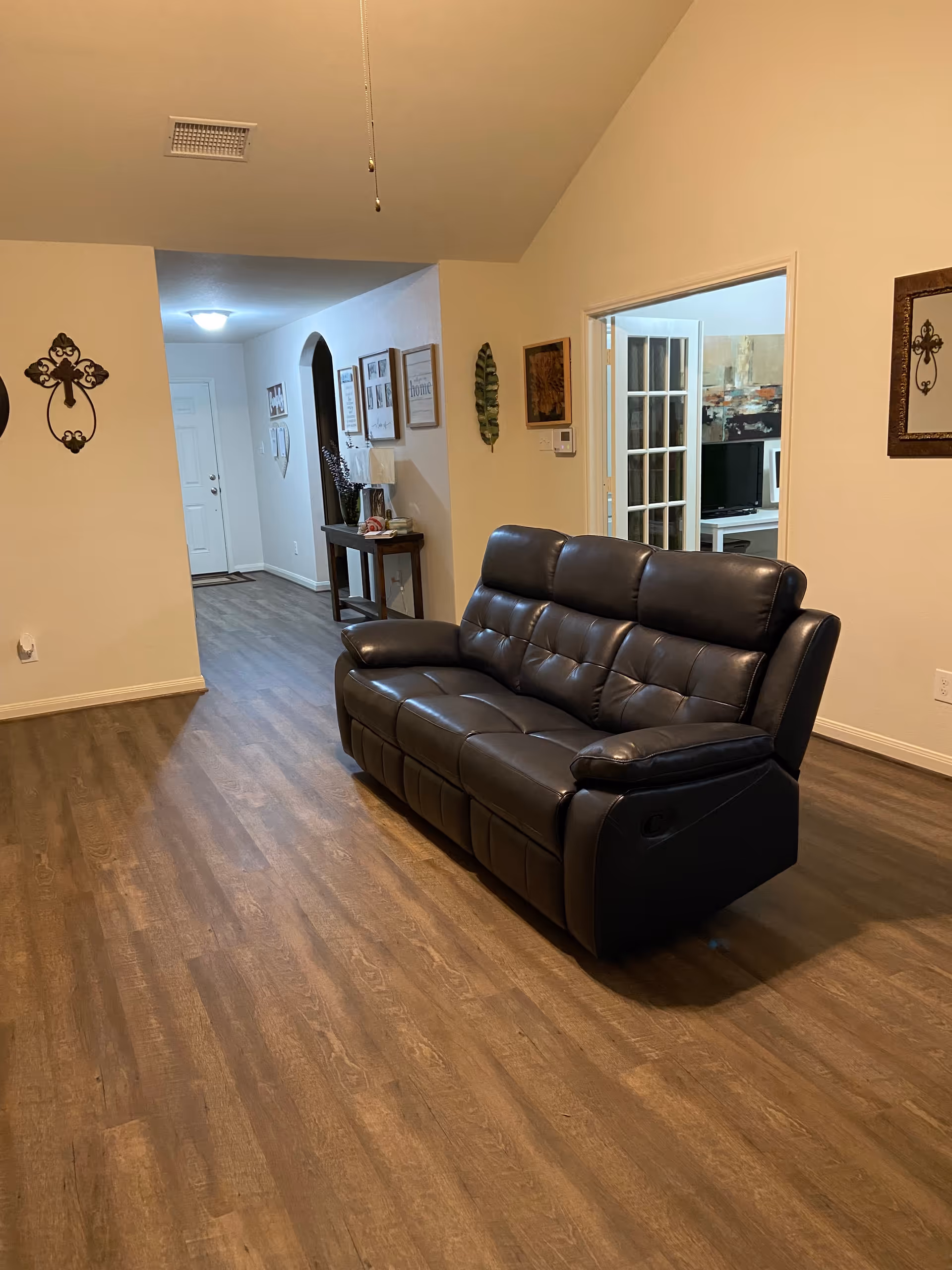 A spacious living room with a black leather sofa and wood floors.