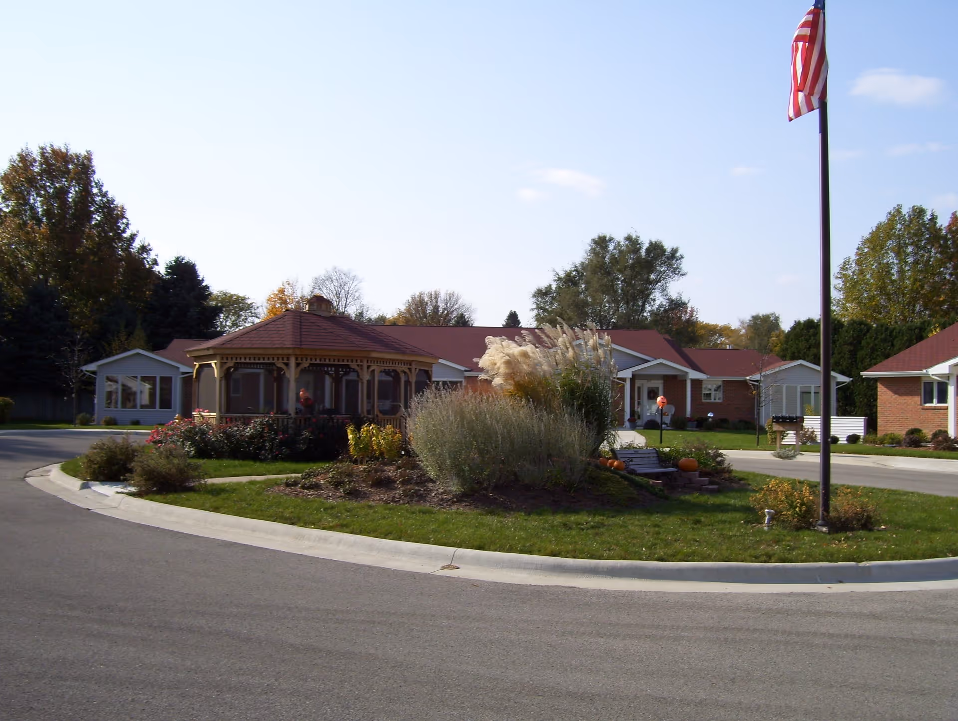 Circular driveway and lawn surround brick buildings and gazebo under a flagpole.