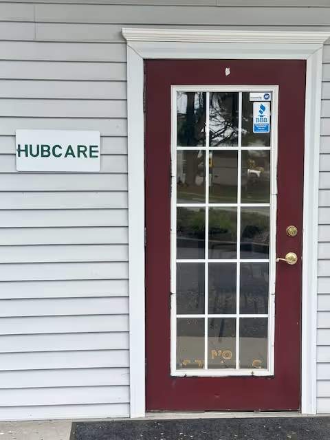 Exterior view of a light gray siding building with a maroon door and HUBCARE sign