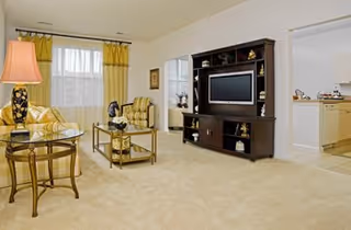 Bright beige living room with yellow-patterned furniture, a TV console, and glass coffee table.