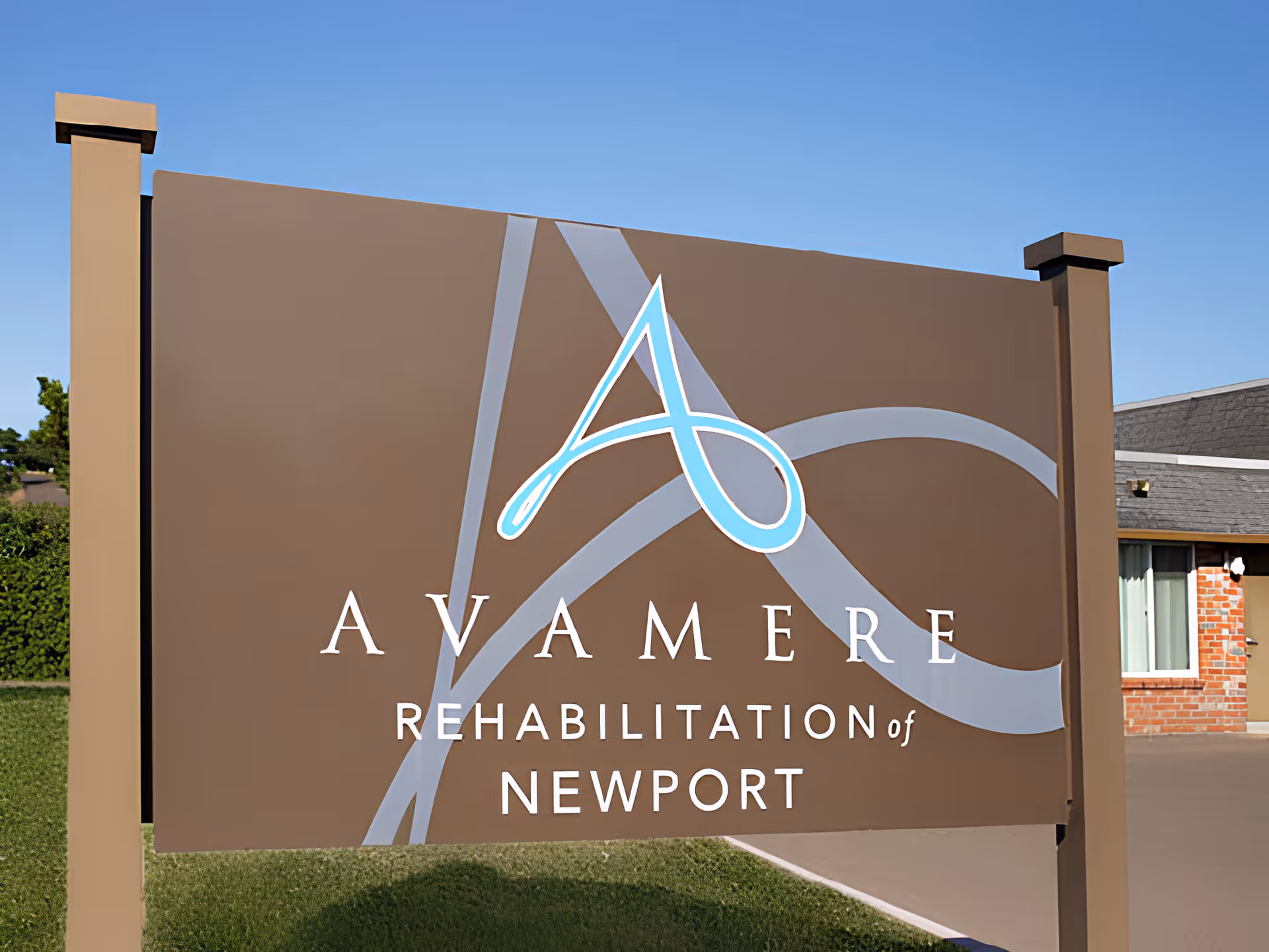 A large brown sign with a blue and white stylized letter A and the text 'Avamere Rehabilitation of Newport' in white letters, situated outdoors with a building and clear blue sky in the background.