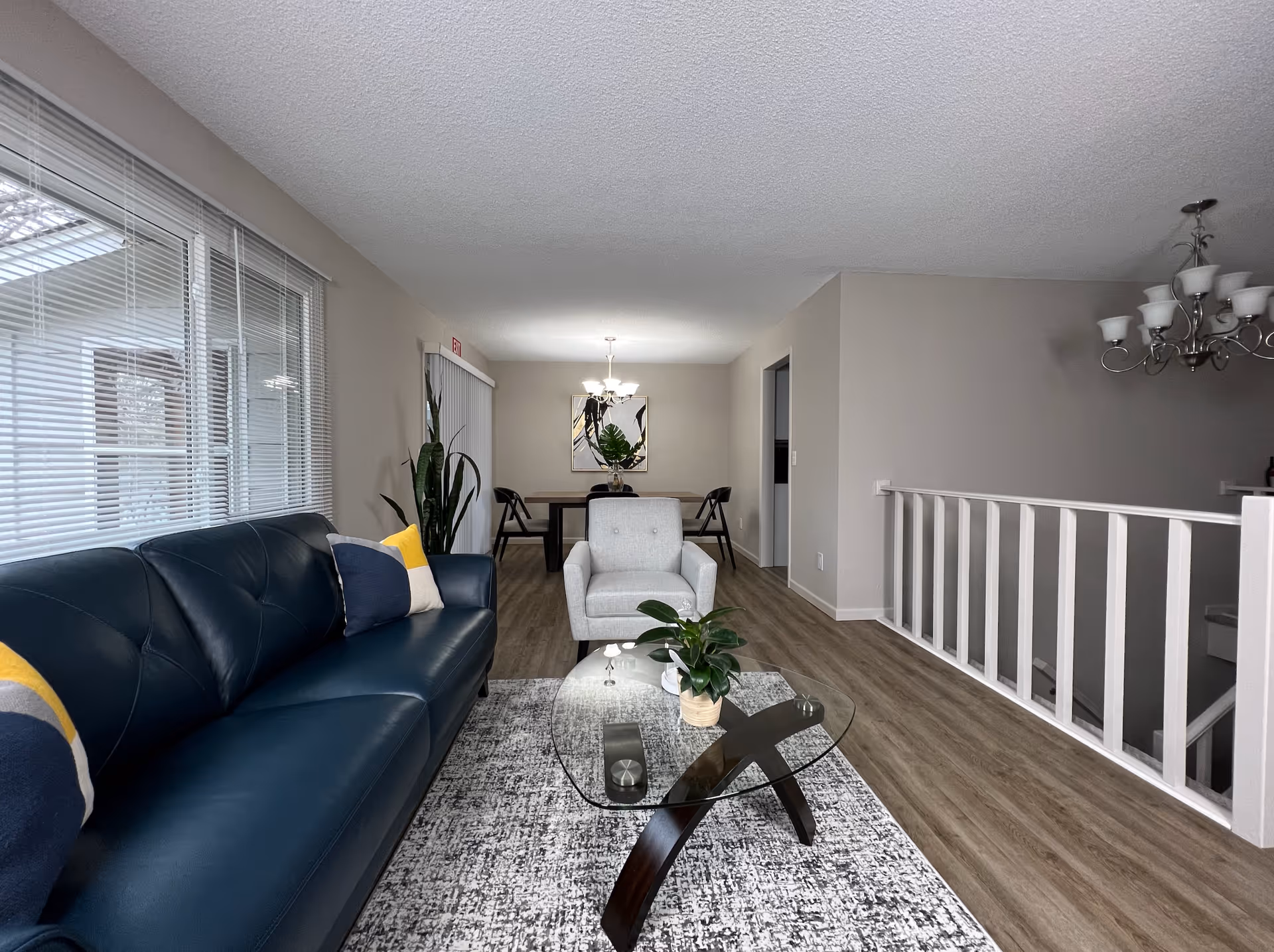 Open living room with blue leather sofa, glass coffee table, and dining area.