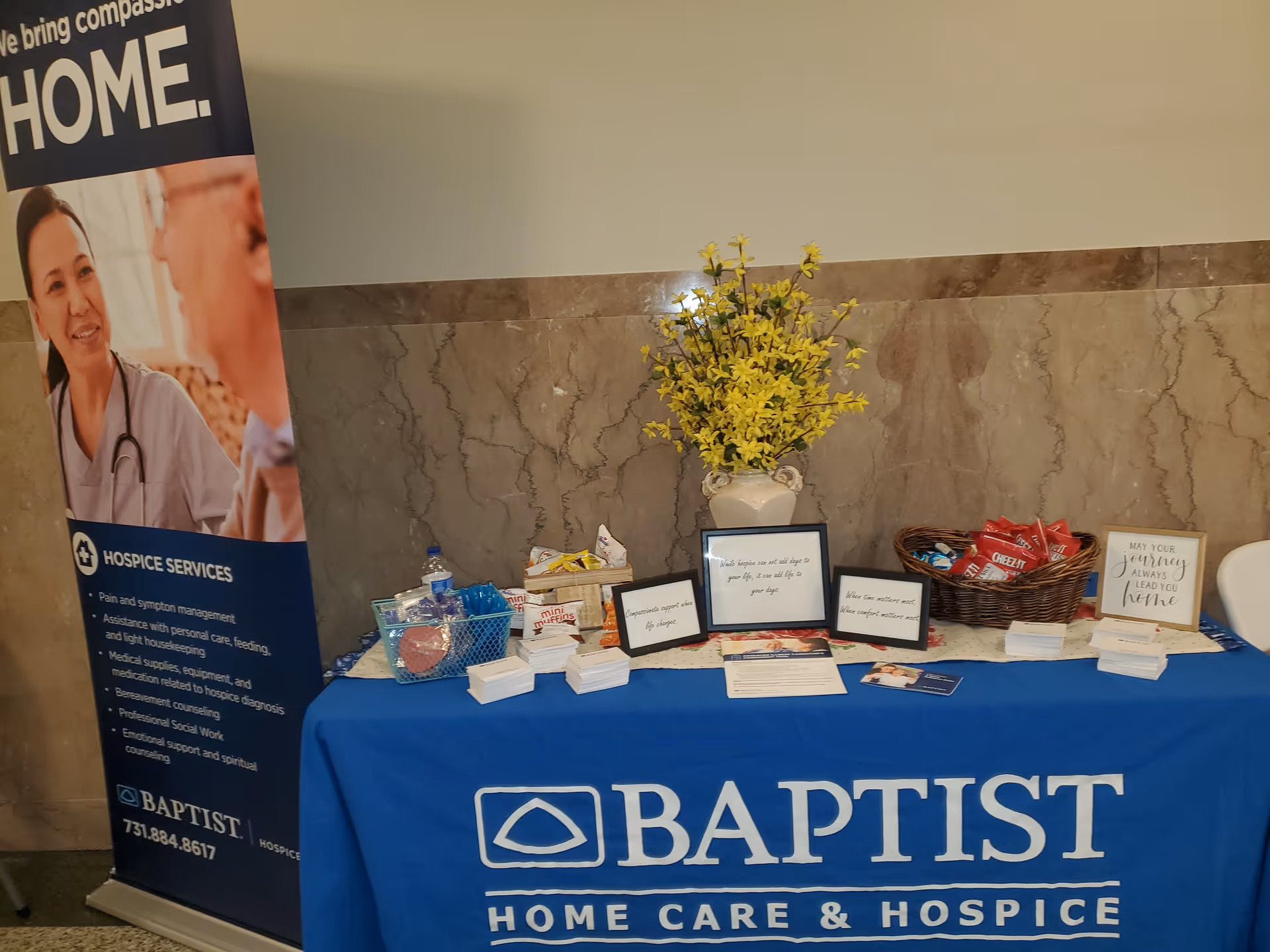 Promotional table for Baptist Home Care & Hospice with banner, flowers, and brochures