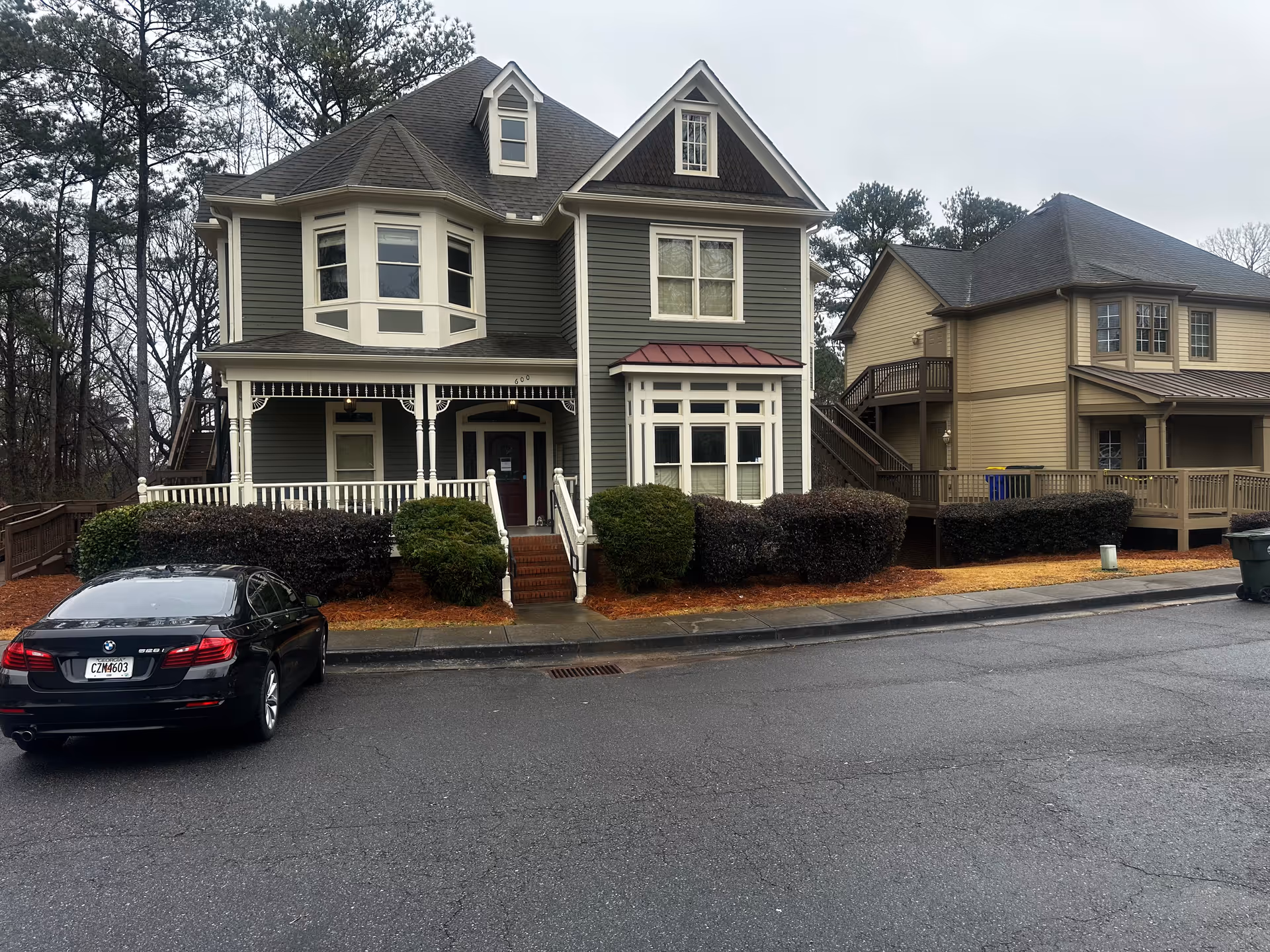 Two-story housefronts with porches, trimmed hedges, and a parked black car.