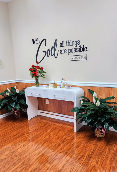 Interior lobby area with a console table, wall quote, and potted plants.