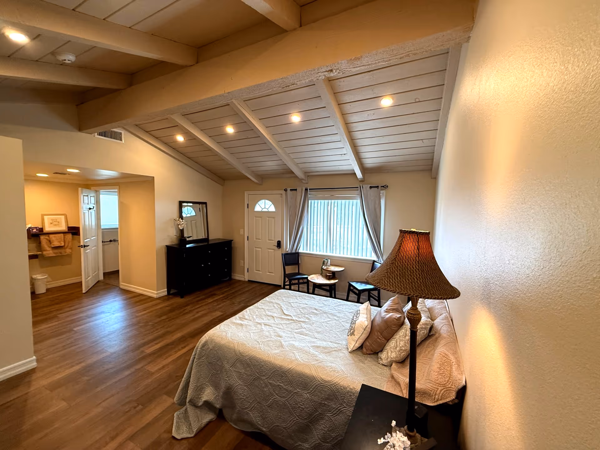 A spacious bedroom with a large bed, dresser, nightstand, and window seating.