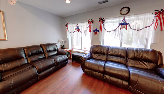 Living room with two dark leather couches, windows, and festive patriotic garlands.