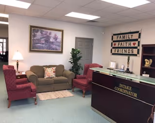 Lobby reception area with seating, an intake coordinator desk, artwork, and a plant.