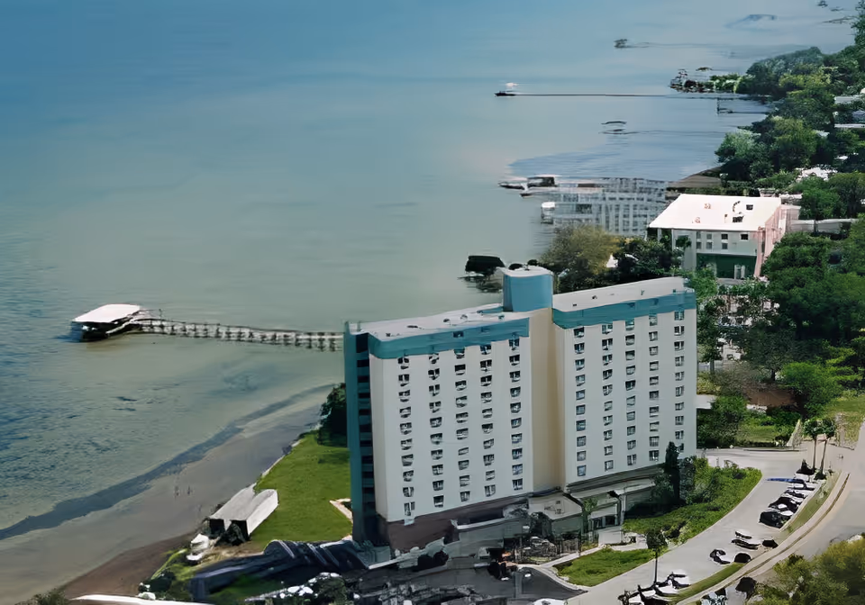 Aerial view of a multi-story assisted living building on the shoreline with a long pier extending into the water and surrounding greenery.