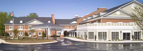 A brick and white-painted senior living facility exterior with glass storefronts and a drive-up entrance.