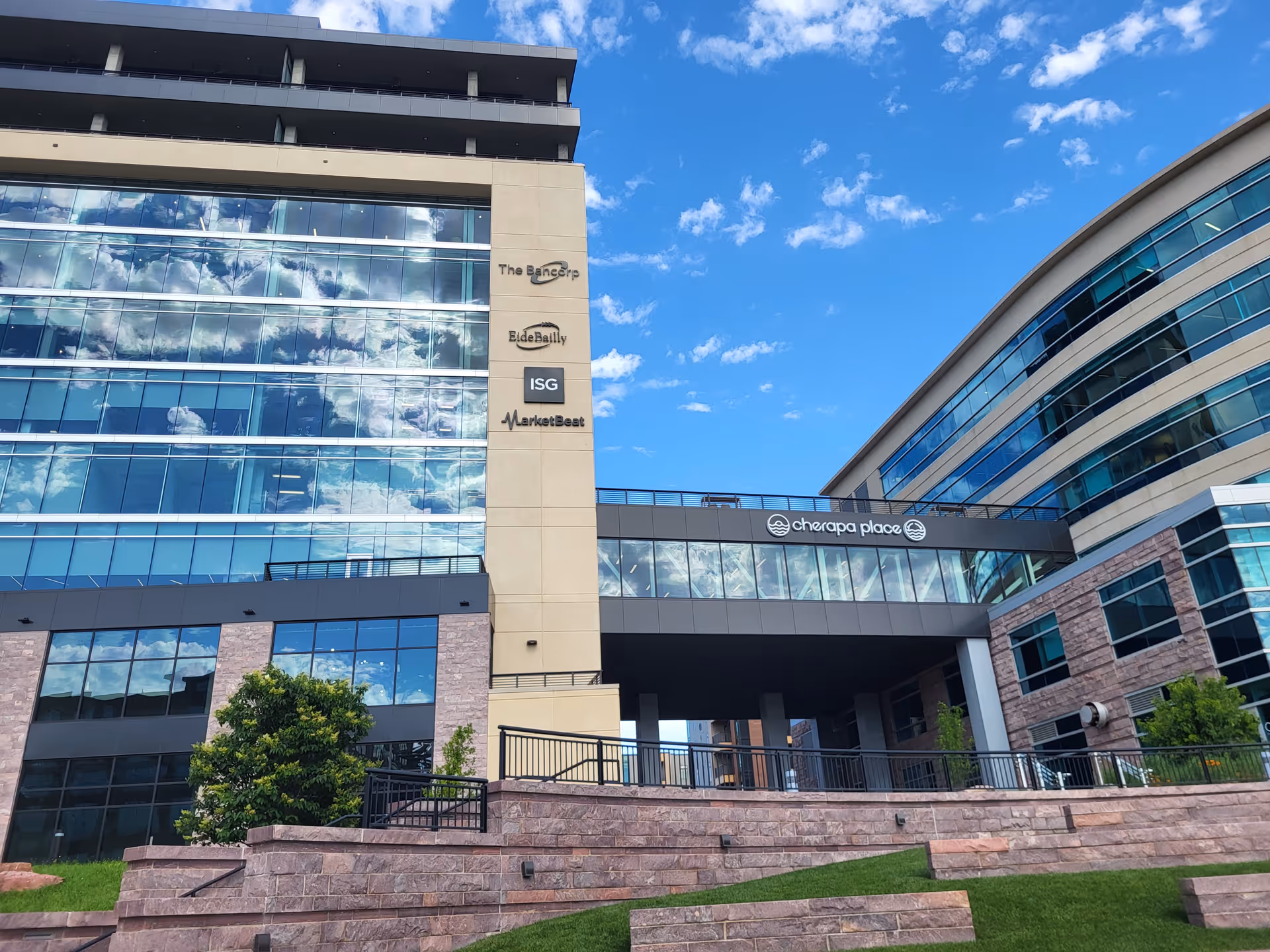 Modern glass-fronted building exterior with multiple logos and a clear blue sky.