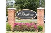 Exterior sign with Woodbine Rehabilitation & Healthcare Center between brick pillars and landscaping.