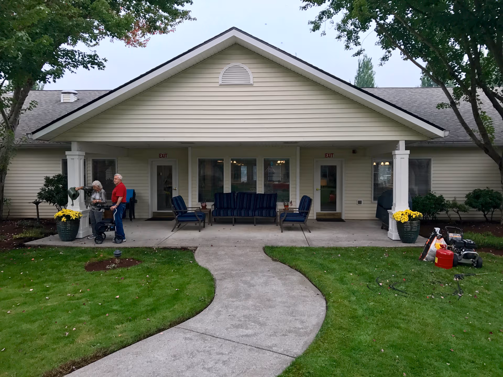 Beige single-story senior living facility with front porch seating and two people outside.