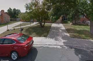 Front yard and driveway of a suburban house with a tree and a red car parked on the street.