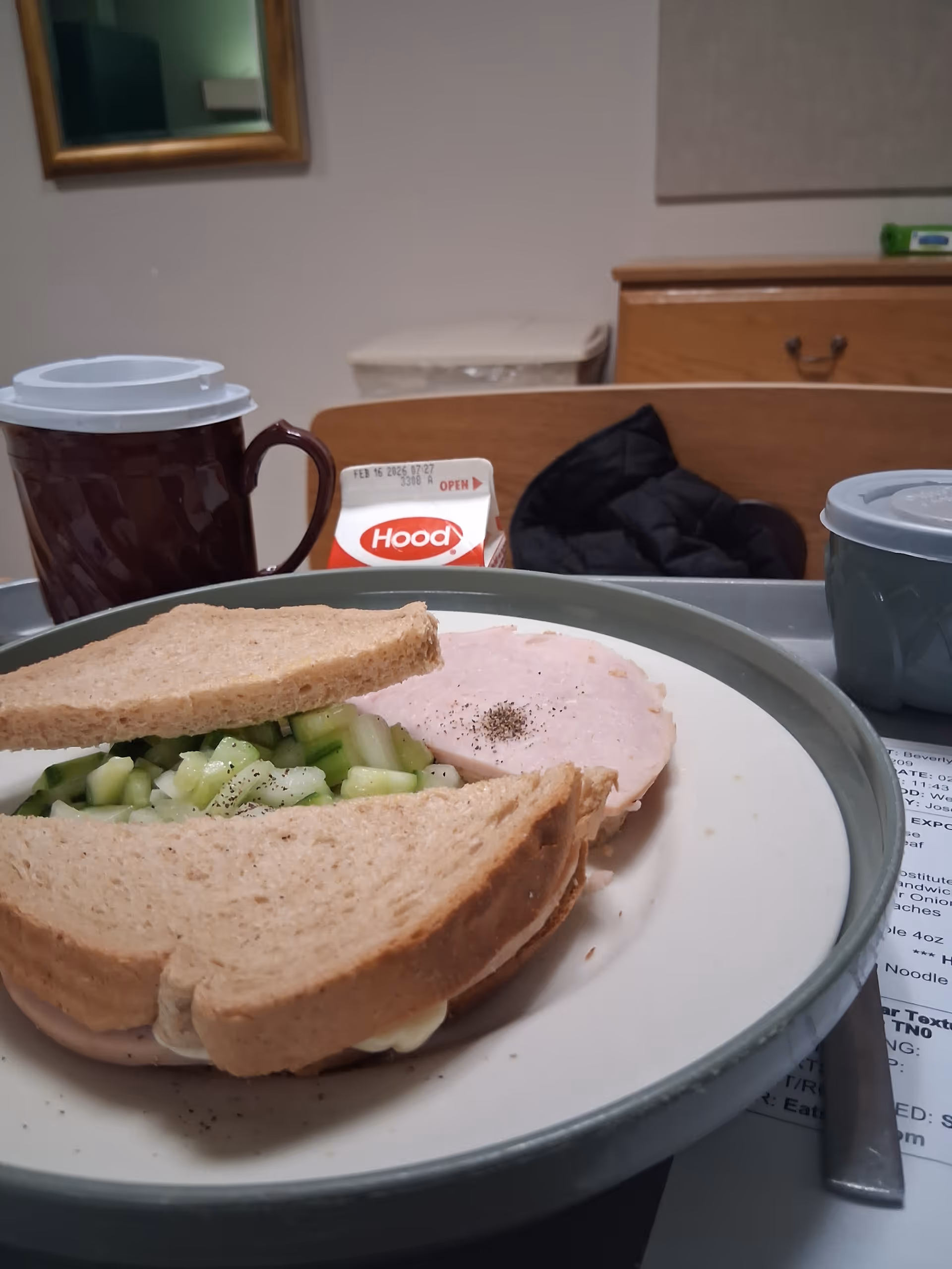 Meal on a tray with sandwich, cucumber, and coffee cup in dining area.